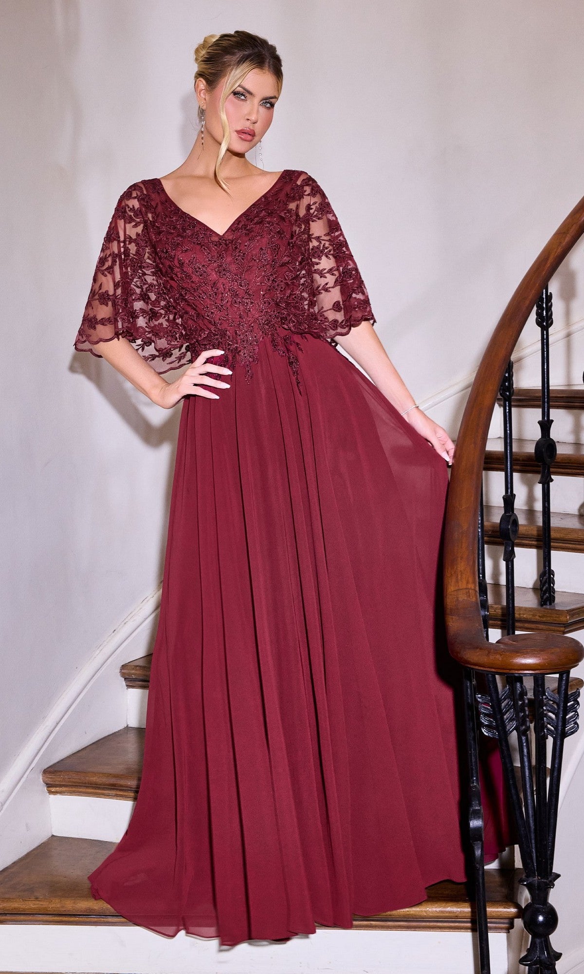 A woman in the Ladivine CL10 Long Formal Dress in burgundy, featuring a lace-embroidered bodice and sheer flutter sleeves, stands on a staircase holding the banister.